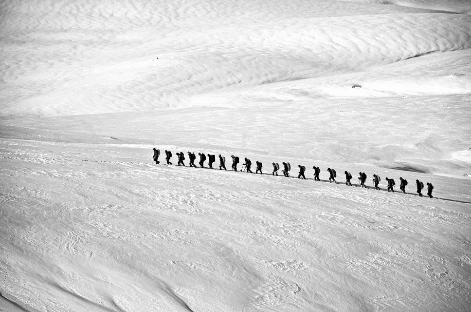 A large group of trekkers traverse the snowclad mountain. 